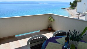 A balcony with a view of the sea, a table with a bottle and glasses, and a potted plant. - Apartments Mistral (Omis)