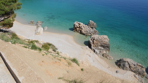 A coastal landscape with clear turquoise waters, rocky outcrops, and a sandy beach. - Apartments Mistral (Omis)