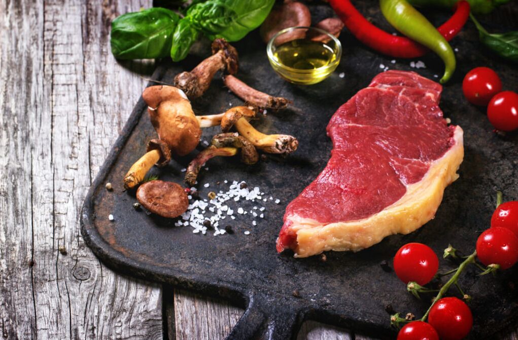 Bife com cogumelos e tomate cereja sobre uma tábua de ardósia.
