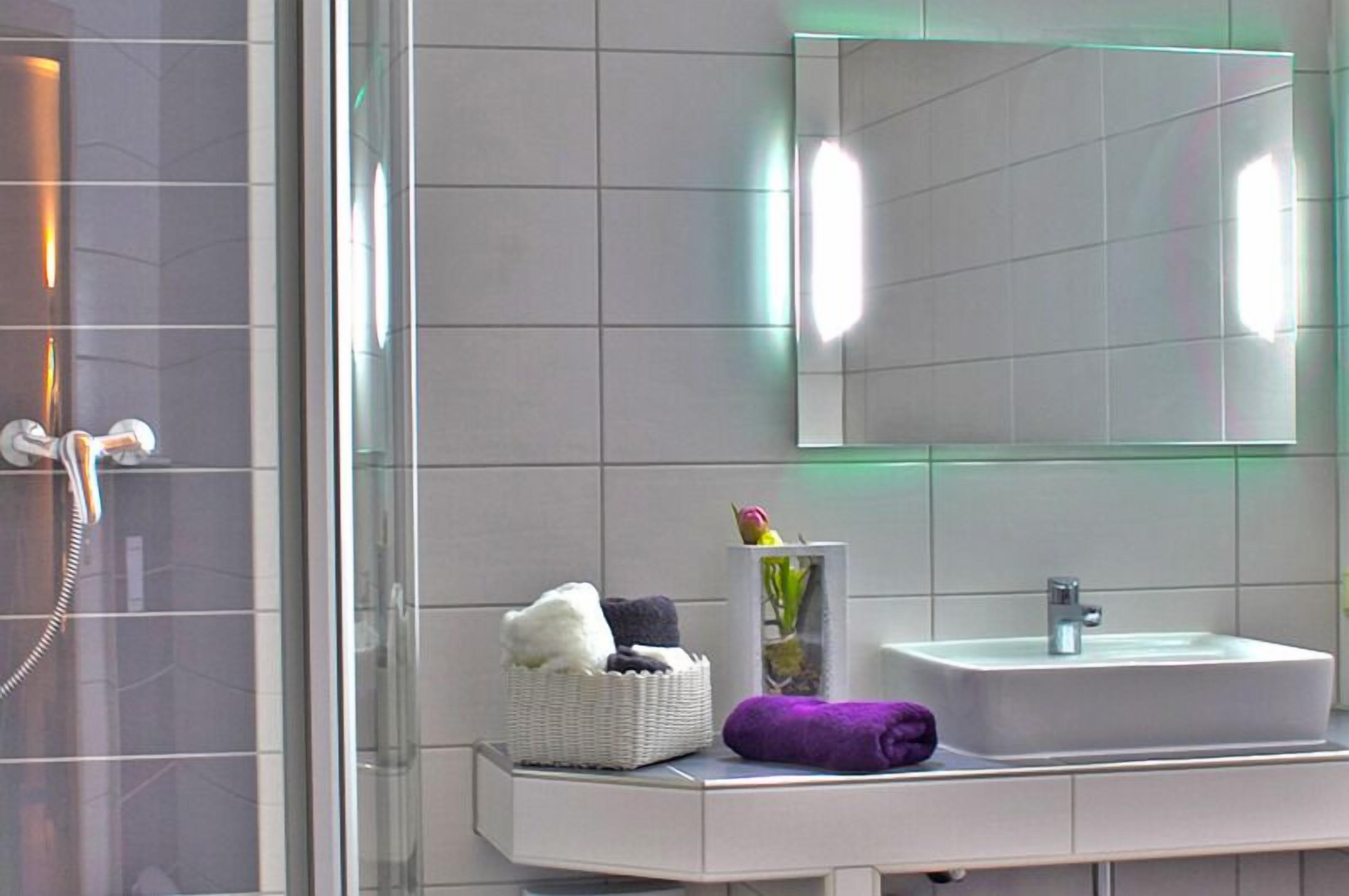 A modern bathroom with a glass shower enclosure, a white sink, and a mirror.