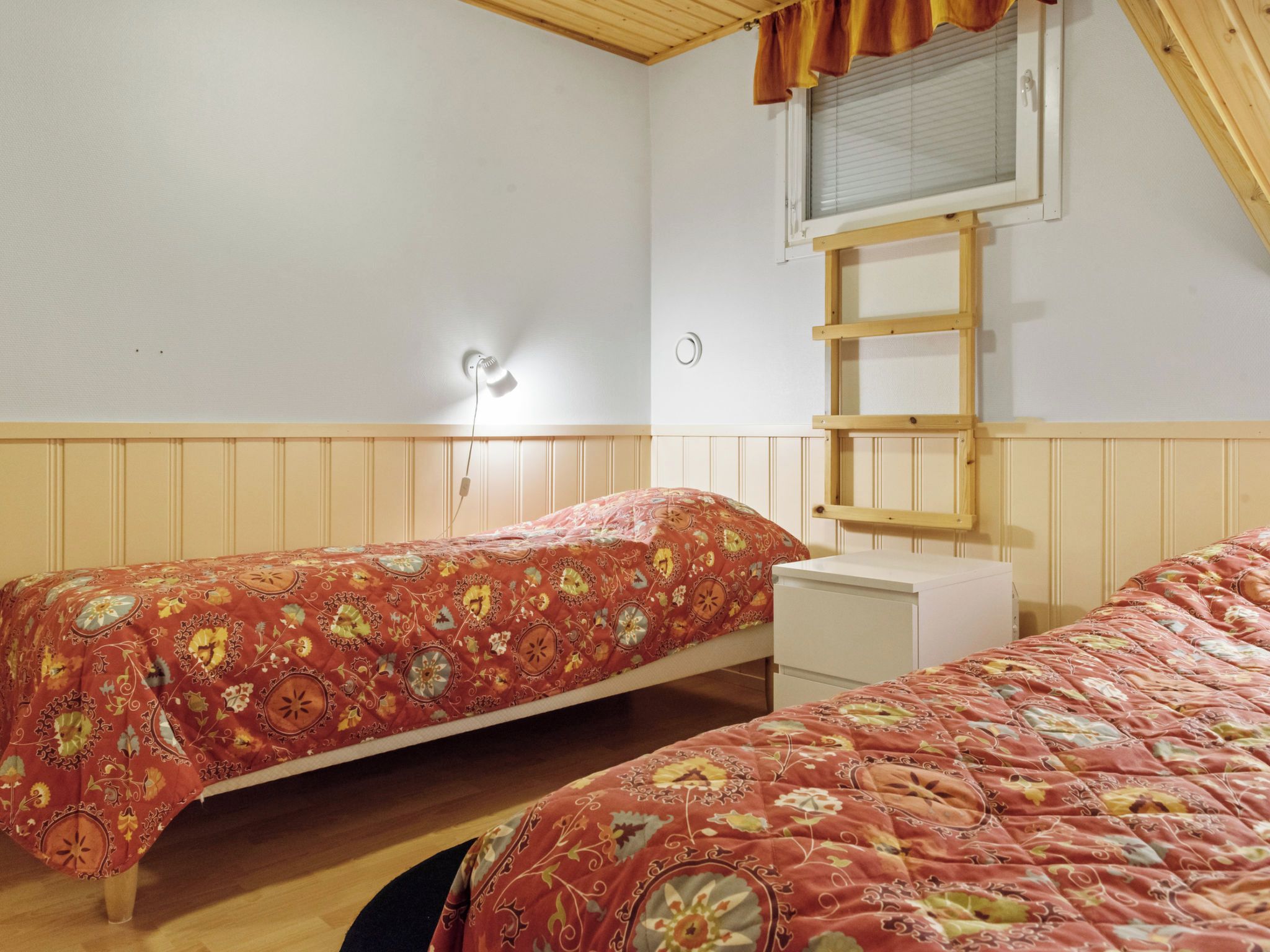Un dormitorio con dos camas individuales, una escalera de madera, una mesita de noche blanca y un aplique de pared.