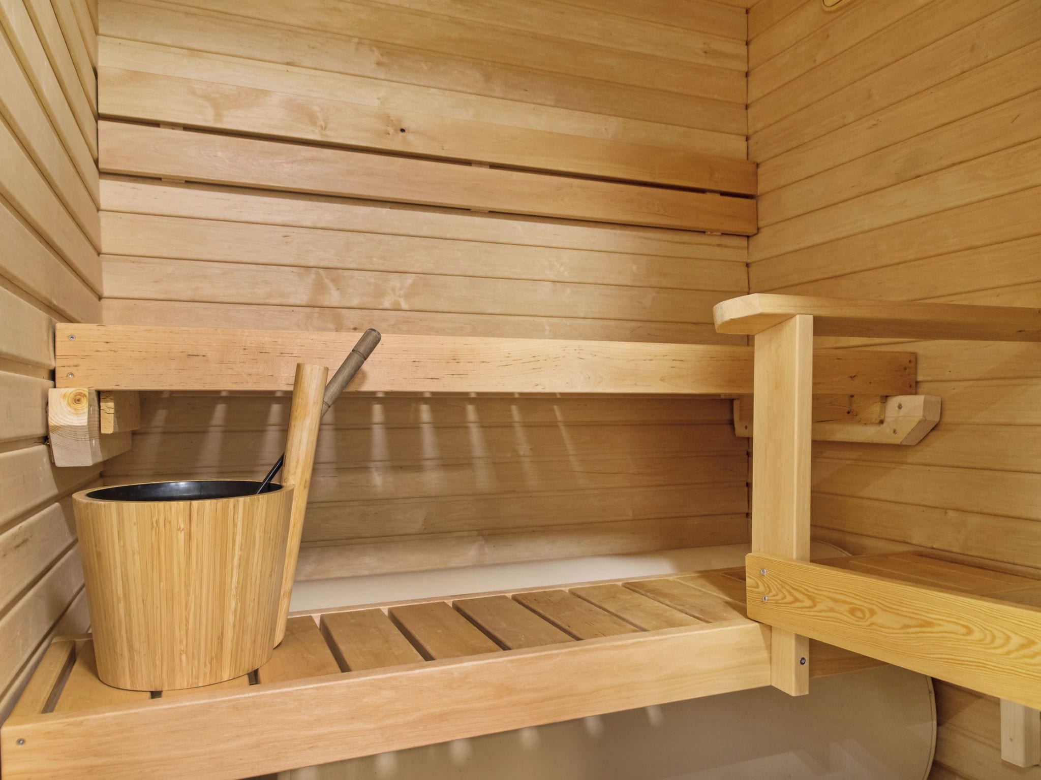 Un sauna avec des bancs en bois, un banc muni d’une serviette et un seau en bois.