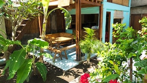 Uma pérgola de madeira com um banco, rodeada por vegetação exuberante e plantas em vasos.