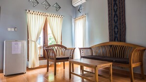 Quarto com sofá de madeira, duas cadeiras, uma mesinha e um frigorífico.
