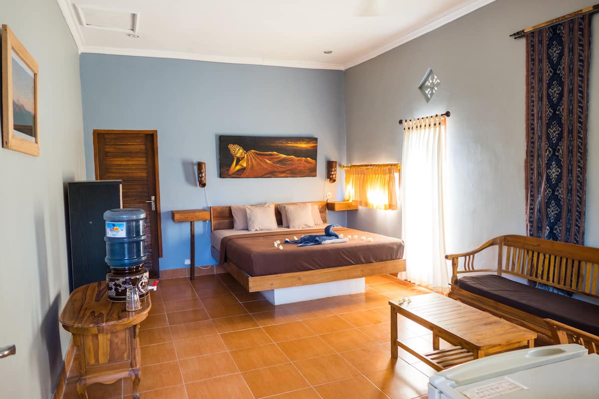 A bedroom with a bed, bedside tables, a water dispenser, a wooden bench, and a painting on the wall.