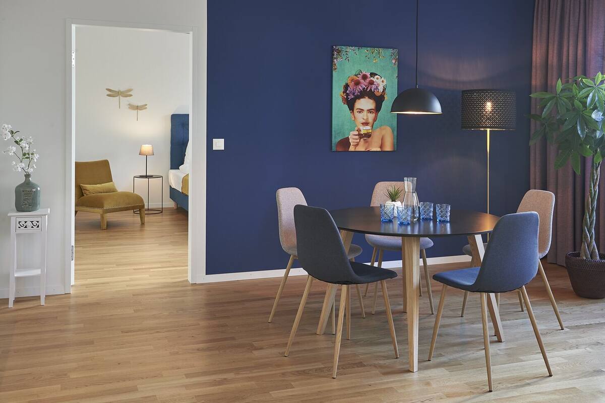 A modern dining area with a round table, four chairs, a floor lamp, and a potted plant.