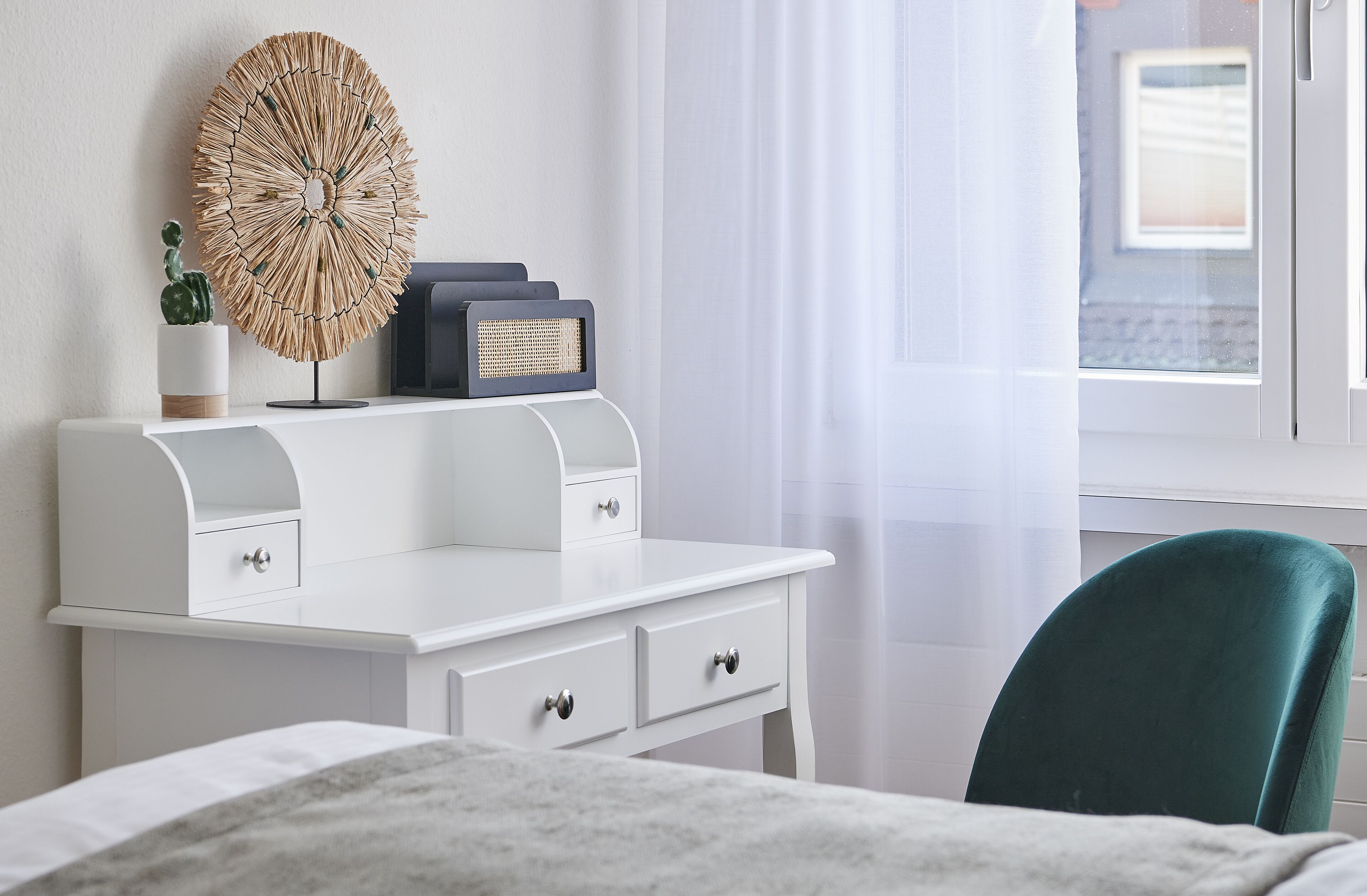 A neatly arranged bedroom with a white dresser, a radio, a cactus, and a green chair.