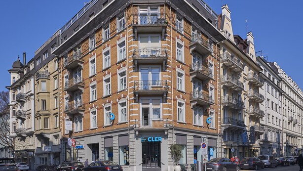 Un edifici de cantonada amb un banc a la planta baixa, diversos balcons i un senyal d'hotel ben visible.