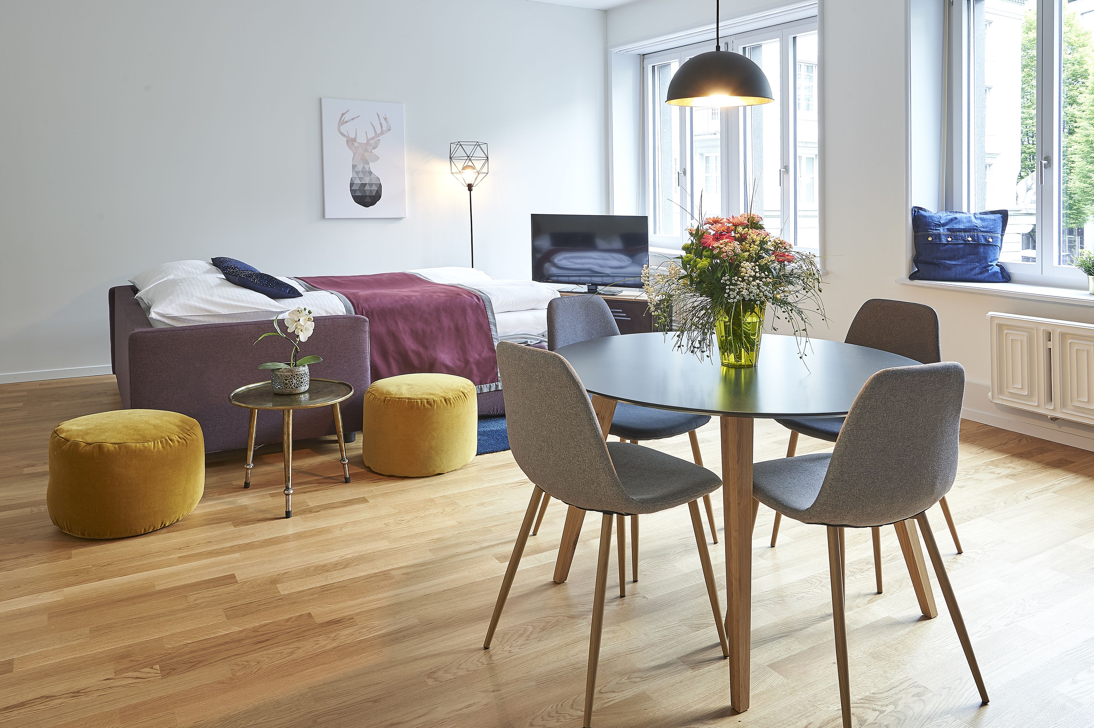A modern room with a bed, a dining table with chairs, a TV, and a window with a view.