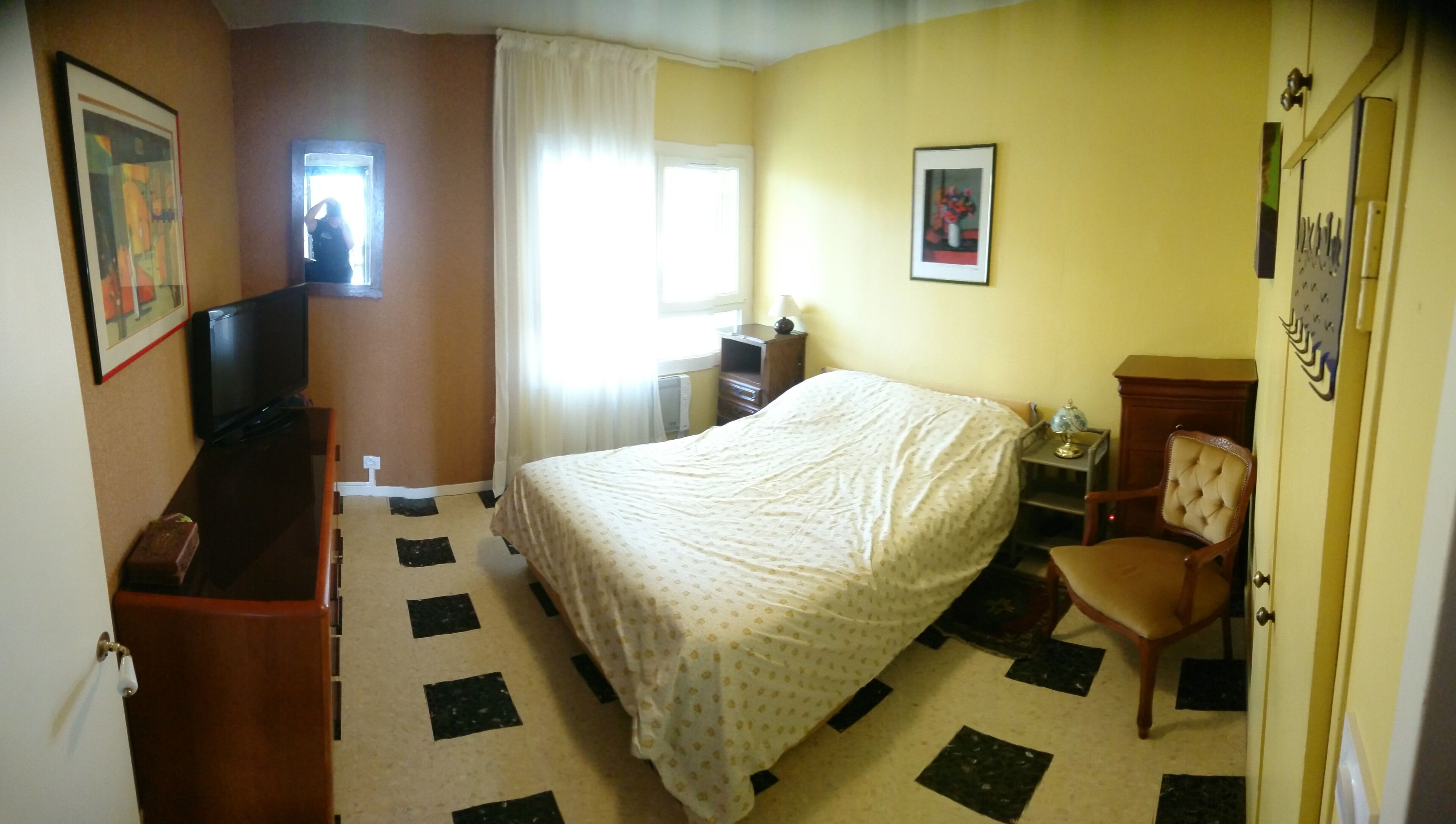 Quarto de hotel com cama, escrivaninha, cadeira, televisão, janela com cortinas e porta.