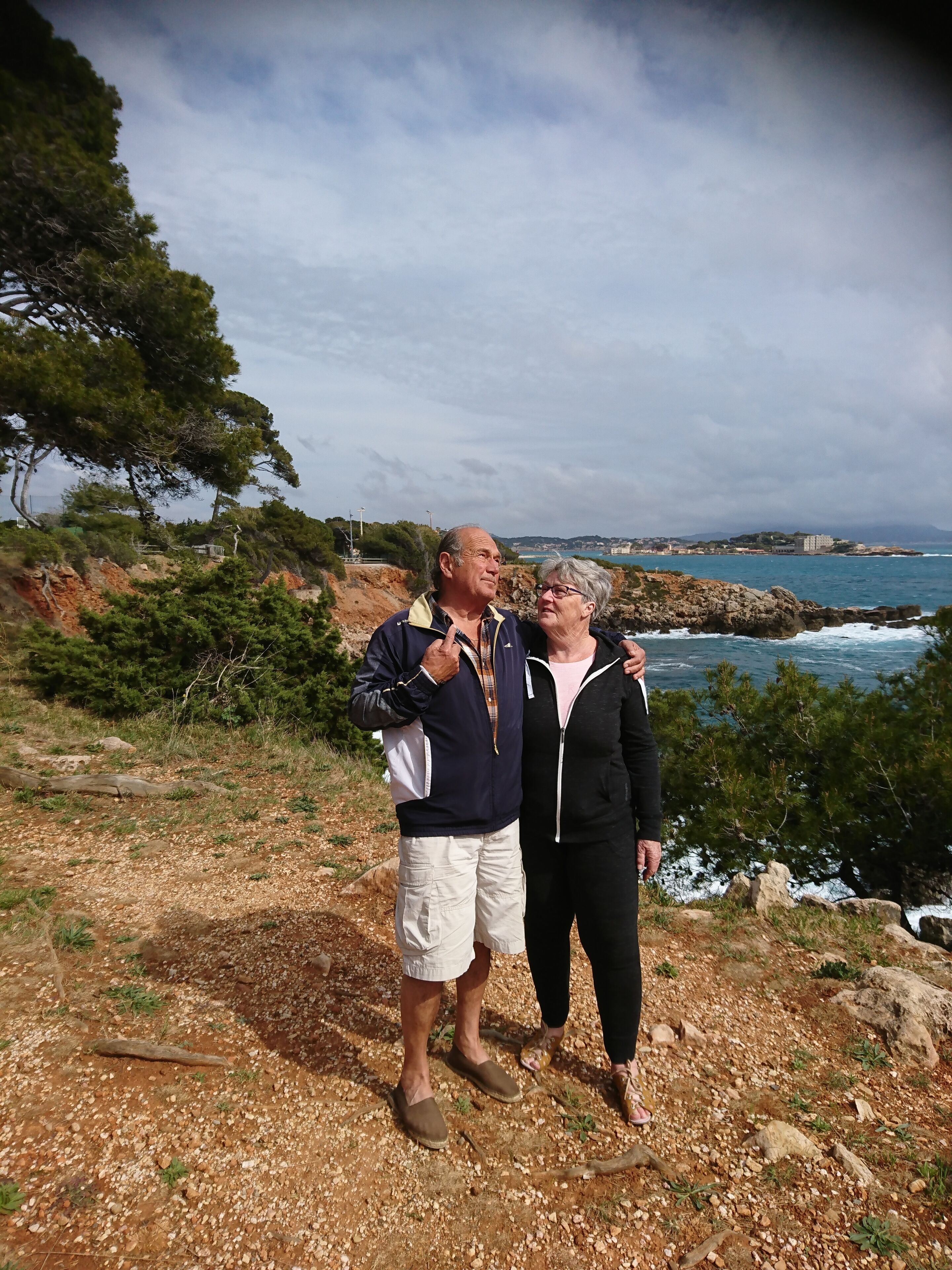 Dos personas sobre terreno rocoso, con vista al mar.