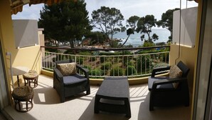 Ein Balkon mit Korbmöbeln, einem kleinen Tisch und Blick auf das Meer und Bäume.