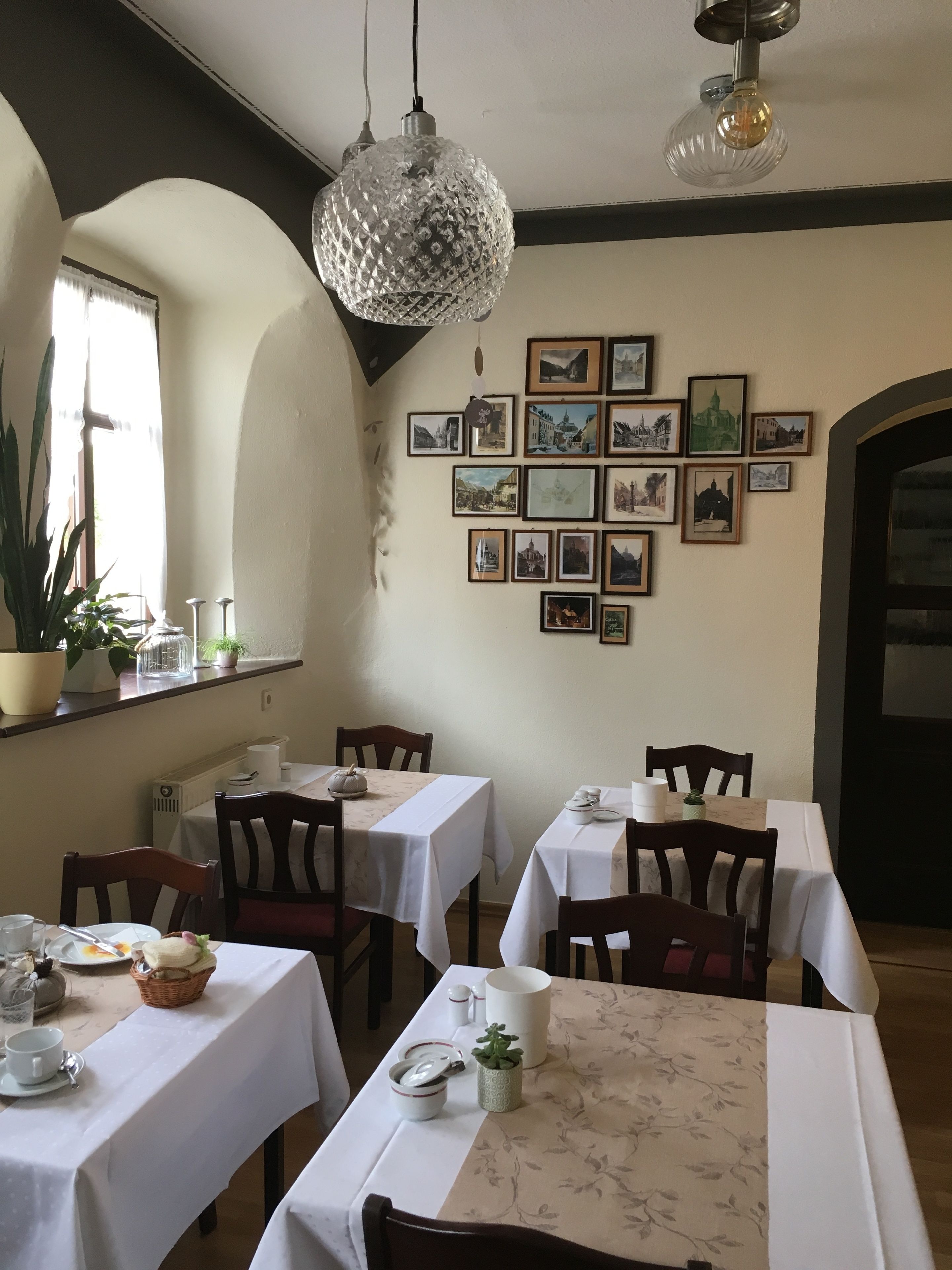 Un espace repas avec des tables dressées pour les repas, des tableaux encadrés accrochés au mur et des luminaires suspendus.
