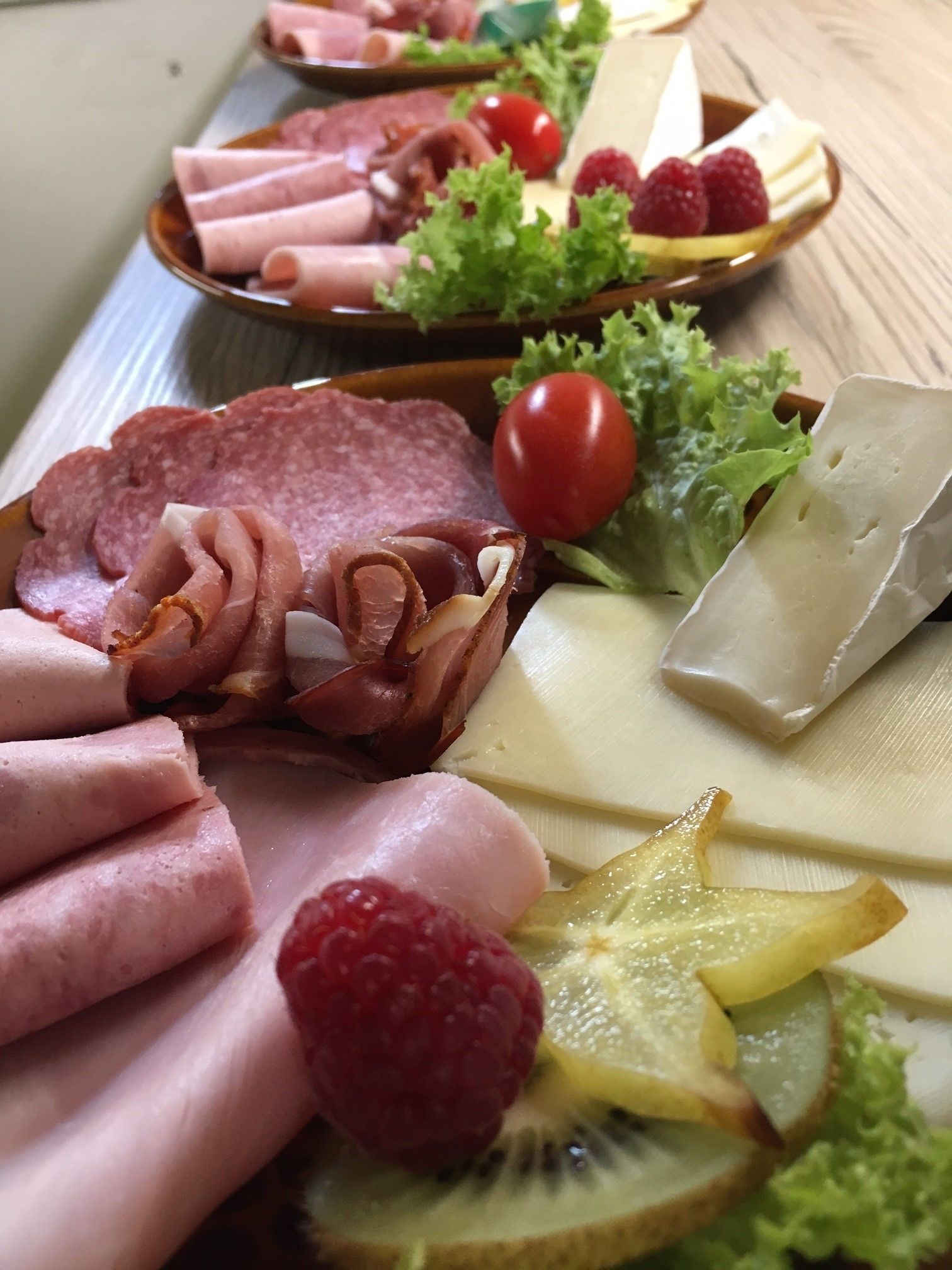 Varietat de carn i formatge tallats sobre una taula de fusta, acompanyats de fruita i verdura.