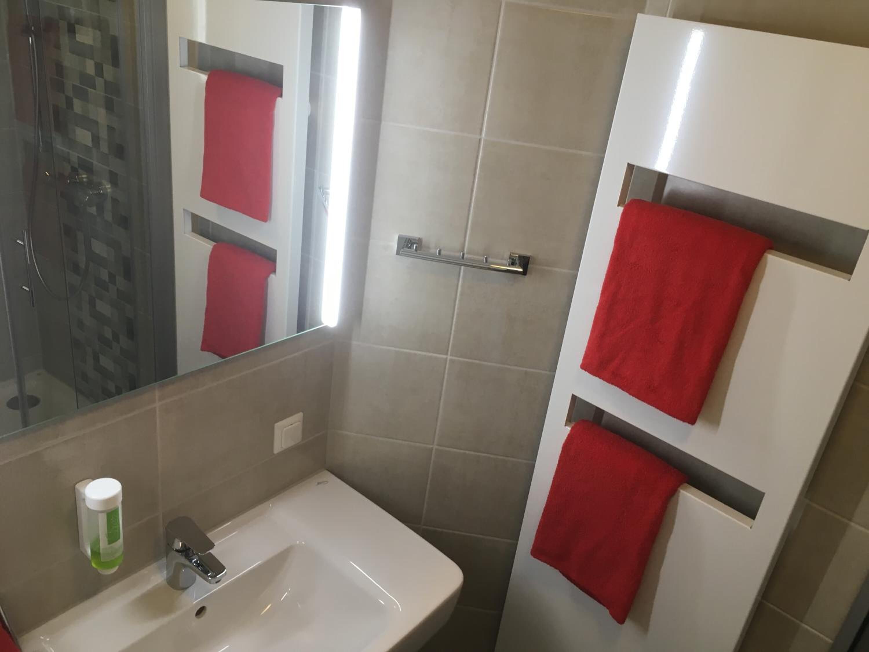 A bathroom with a white sink, a glass shower enclosure, and a mirror reflecting a red towel.