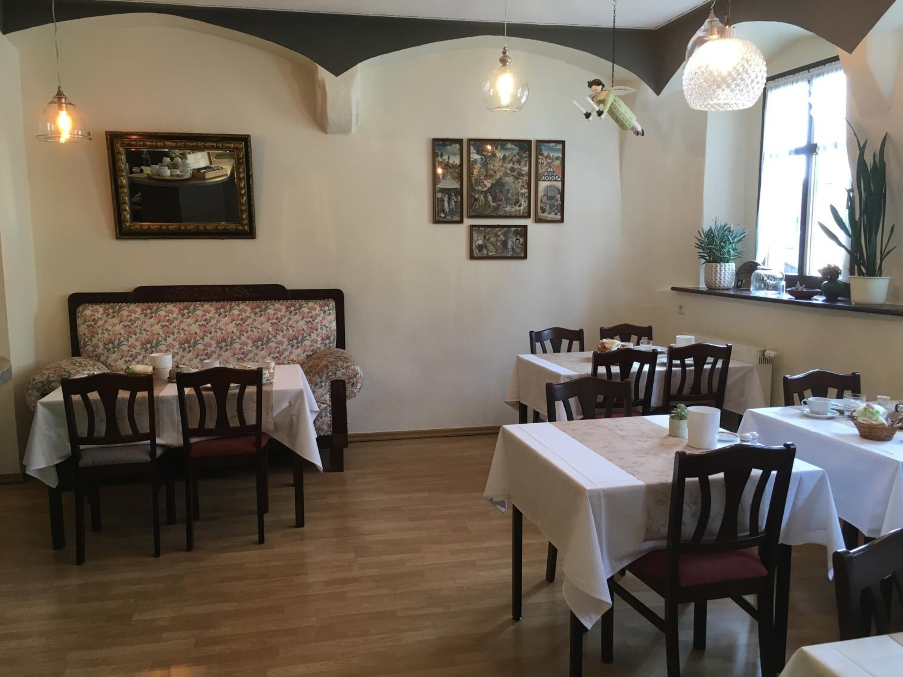 Uma sala de jantar com mesas e cadeiras de madeira, um painel de cama com motivos florais e obras de arte nas paredes.