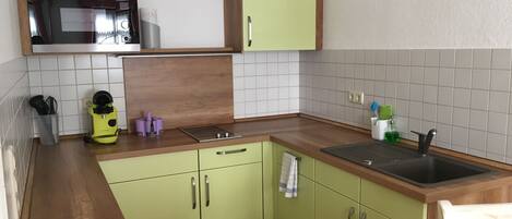 A compact kitchen with a microwave, a sink, and green cabinets.