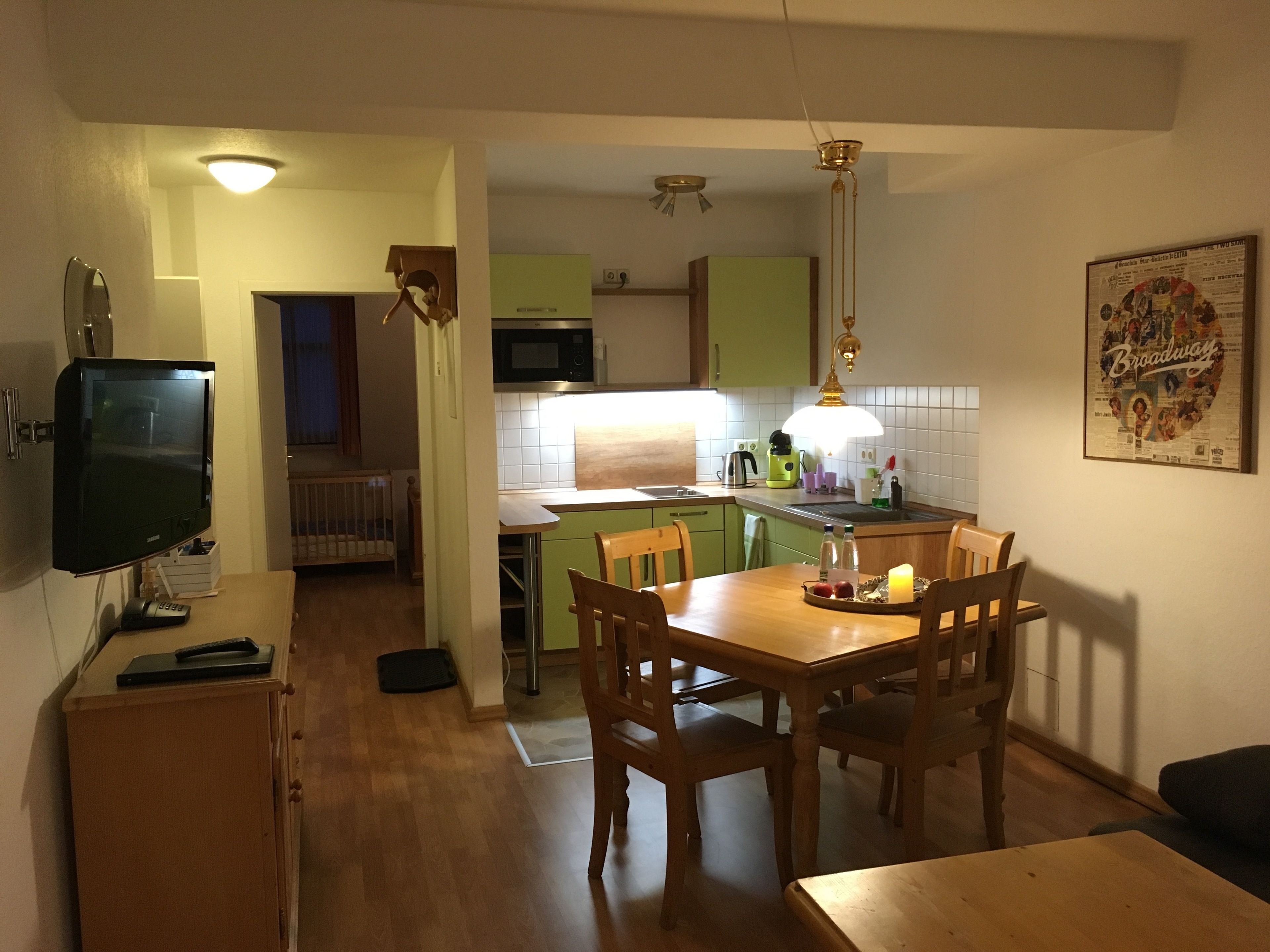 A compact kitchen with a dining area, a television, and a ceiling light fixture.