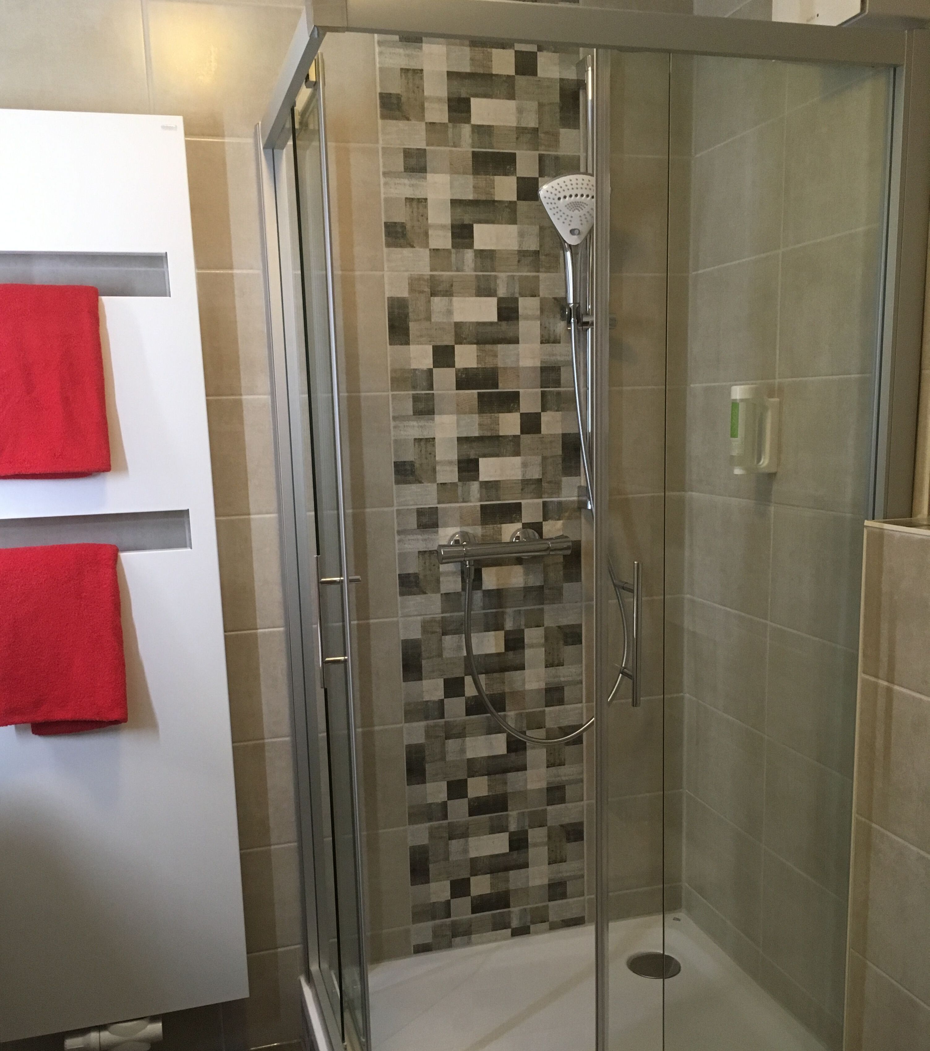 A glass-enclosed shower with a checkered tile wall, a handheld showerhead, and a handheld showerhead.
