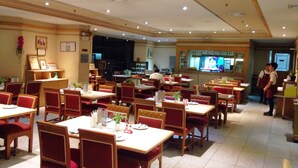 A restaurant with multiple tables and chairs, a counter with staff, and a television screen displaying a program. - Lee Place Hotel (Bangkok)