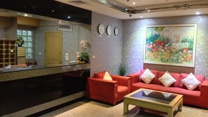 A lobby with a reception desk, a red sofa set, a coffee table, and a large floral painting on the wall. - Lee Place Hotel (Bangkok)