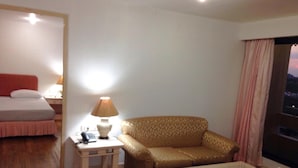 A hotel room with a bed, a sofa, a small table, a lamp, and a window with curtains. - Lee Place Hotel (Bangkok)