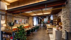 A modern restaurant with exposed brick walls, wooden ceilings, and a stone fireplace. - Garda Hotel (Szombathely)