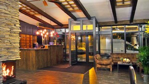 A lobby with a stone fireplace, wooden reception desk, and seating area with a view of the street. - Garda Hotel (Szombathely)