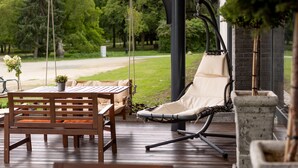 A wooden deck with a table and chairs, a hanging chair, and a stone planter. - Garda Hotel (Szombathely)