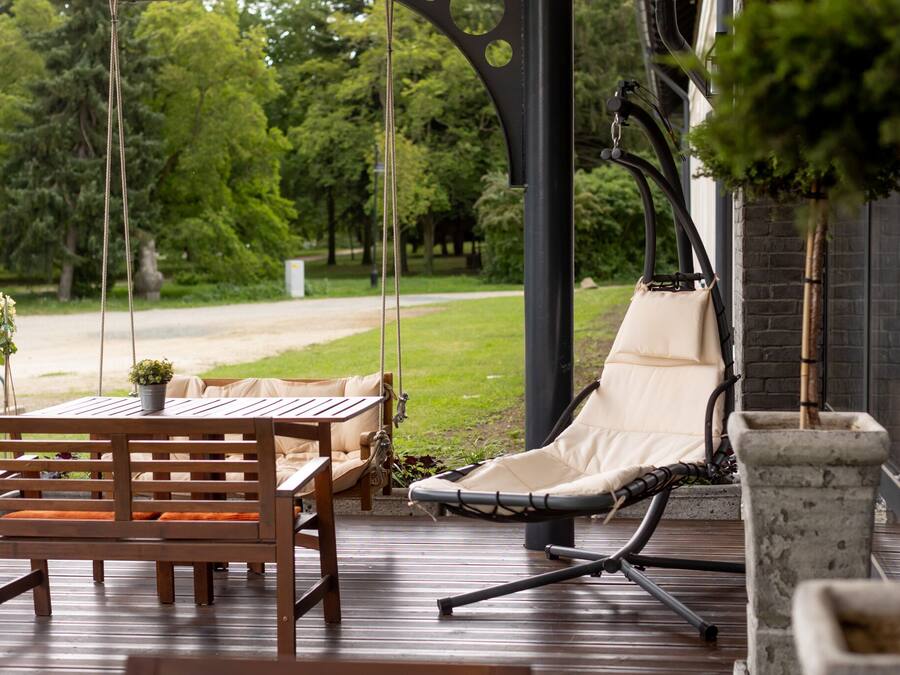 Una terraza de madera con una mesa, sillas y una mecedora colgante, además de una jardinera de piedra.