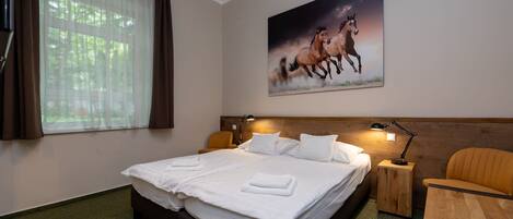 A hotel room with a large bed, two bedside tables, a chair, a painting of horses, and a window with curtains.