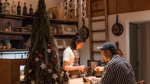 A kitchen area with a Christmas tree, shelves with bottles, and a person using a smartphone. - Uns B&B (Kaohsiung)