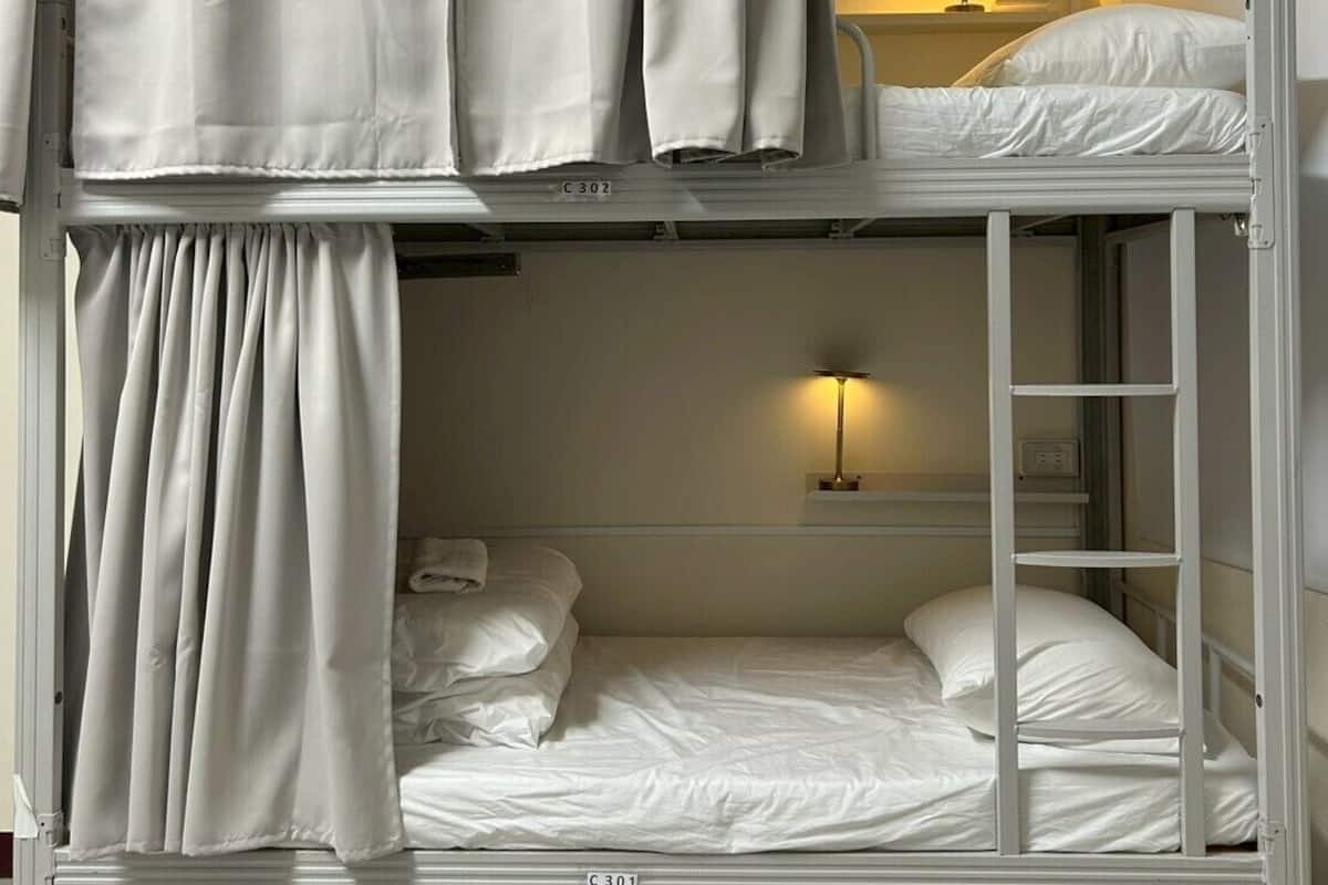 A bunk bed room with curtains, a bedside lamp, and a small shelf.