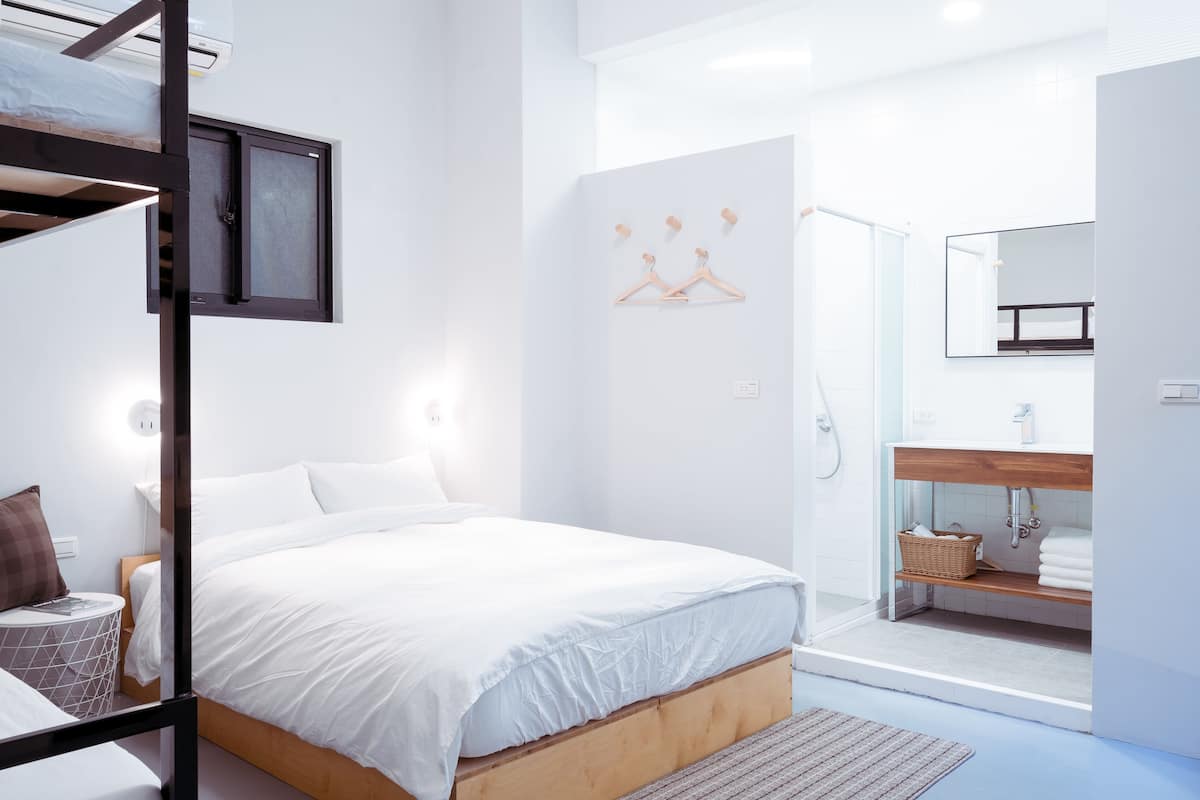 A modern hotel room with a bed, a wooden headboard, a bathroom with a mirror, and a shower area.