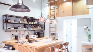 A modern kitchen with wooden cabinetry, a central island with bar stools, pendant lighting, and a variety of kitchen appliances and utensils. - Uns B&B (Kaohsiung)