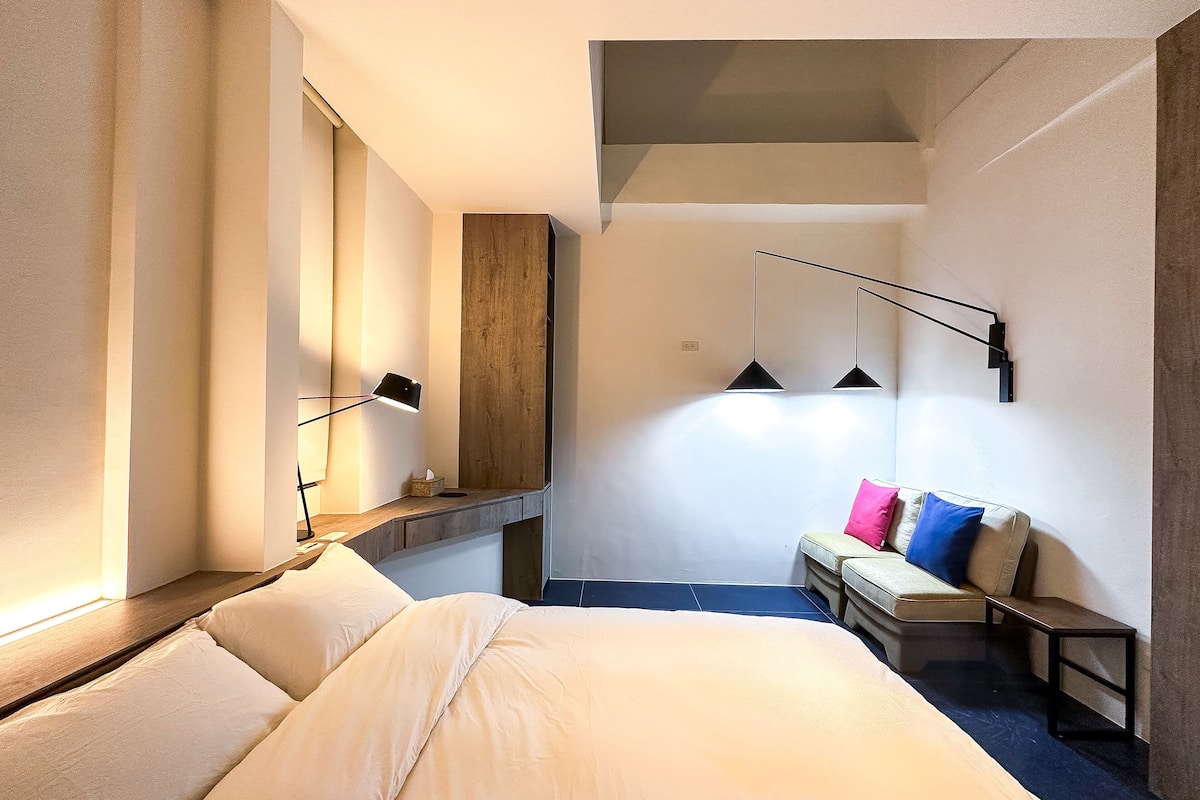 A hotel room with a bed, a bench, a desk, and a mirror.