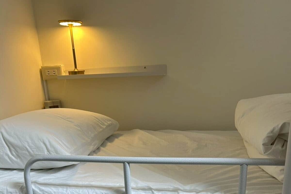 A bunk bed with white bedding and a bedside lamp.