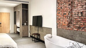 A modern bathroom with a freestanding bathtub, a wooden wardrobe, a flat-screen TV mounted on the wall, and a brick accent wall. - Uns B&B (Kaohsiung)