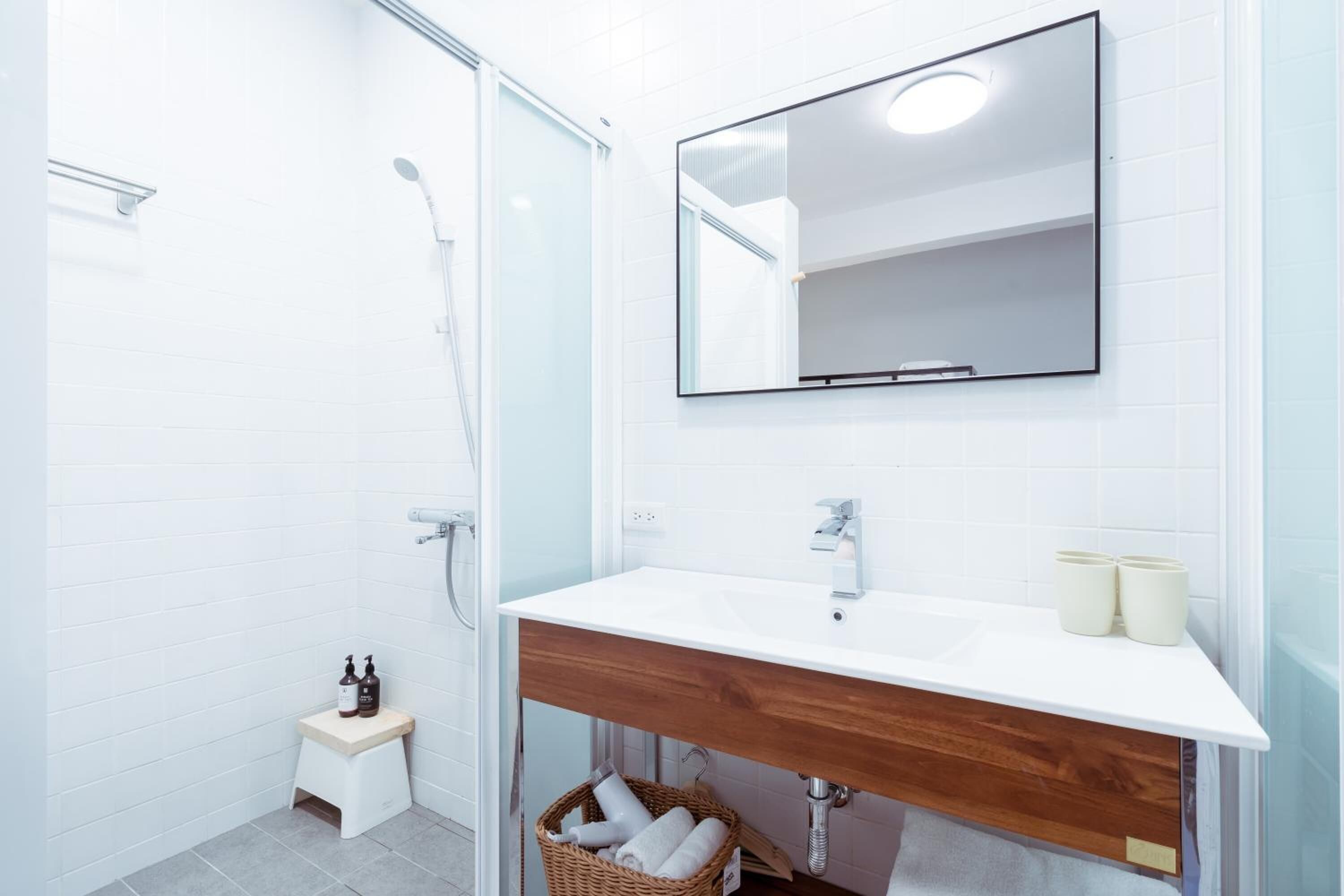 A modern bathroom with a white sink, wooden vanity, and a large mirror.