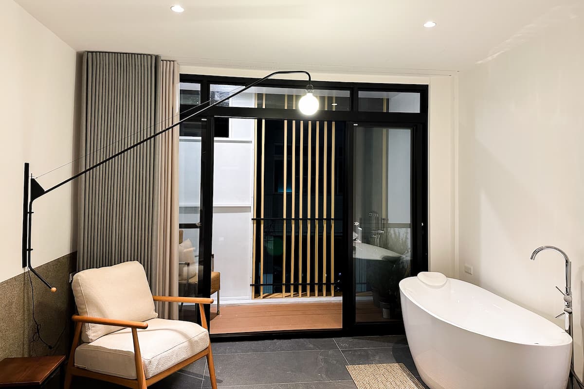 A modern bathroom with a freestanding bathtub, a wooden chair, and a floor lamp.