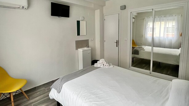 A hotel room with a bed, a TV, a mirror, a wardrobe, and a chair.
