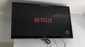 A black television with the Netflix logo on the screen, mounted on a white wall.