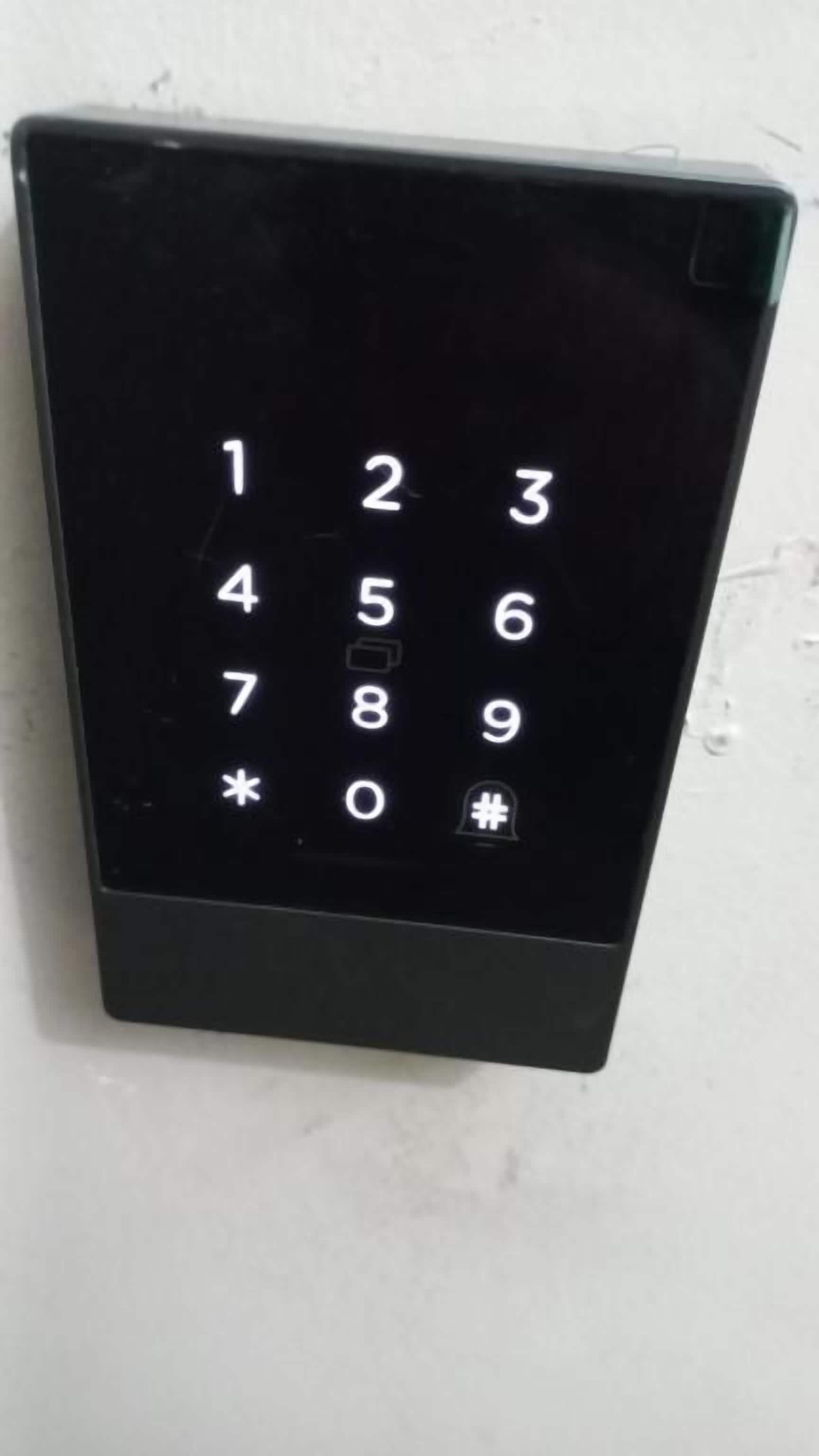 A black numeric keypad mounted on a white wall.