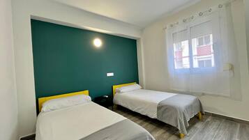 Habitación de hotel con dos camas individuales, una pared de acento verde, una ventana con vistas y una lámpara en el techo.