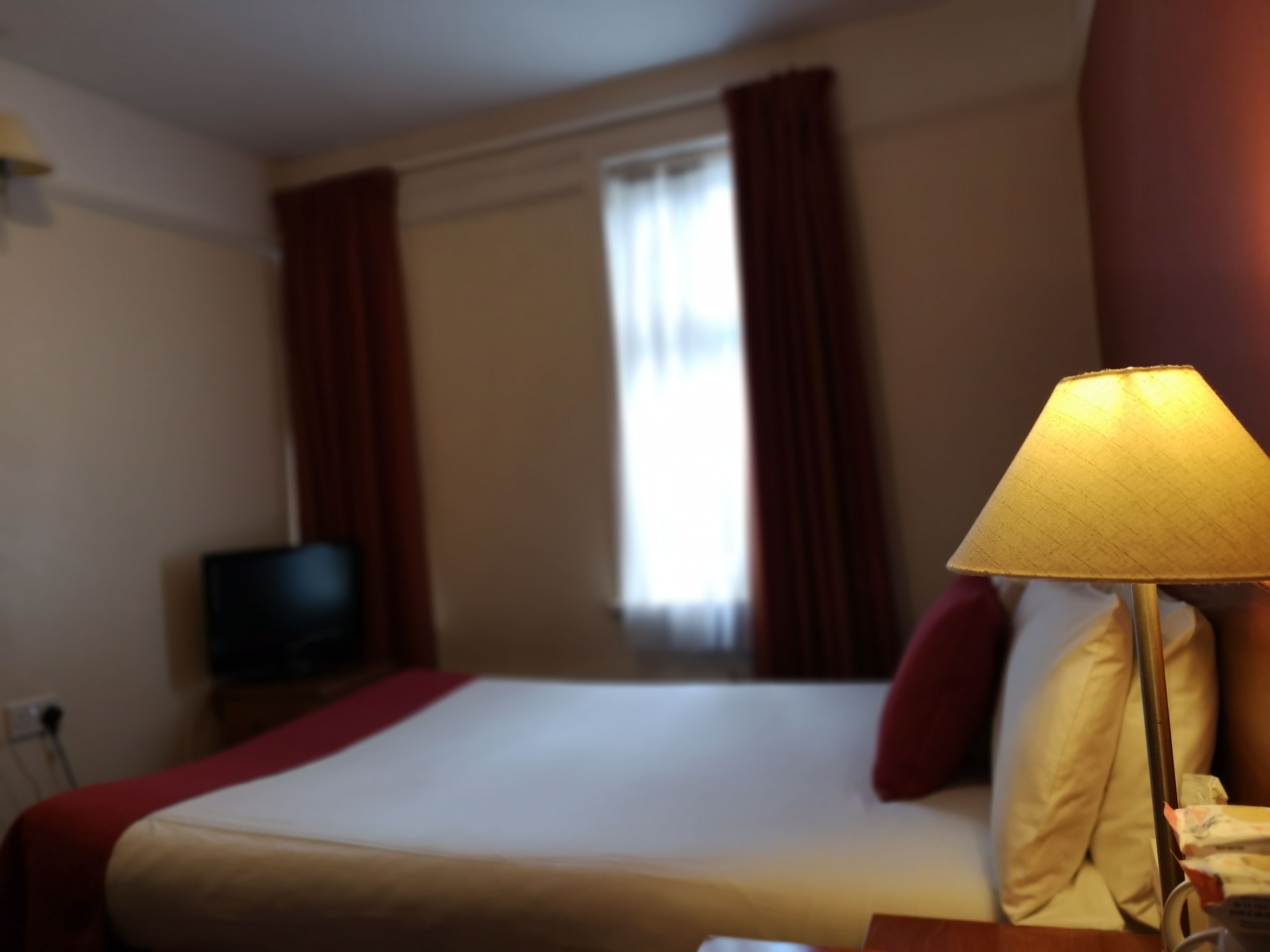 Et hotelværelse med seng, fjernsyn, lampe og gardiner.