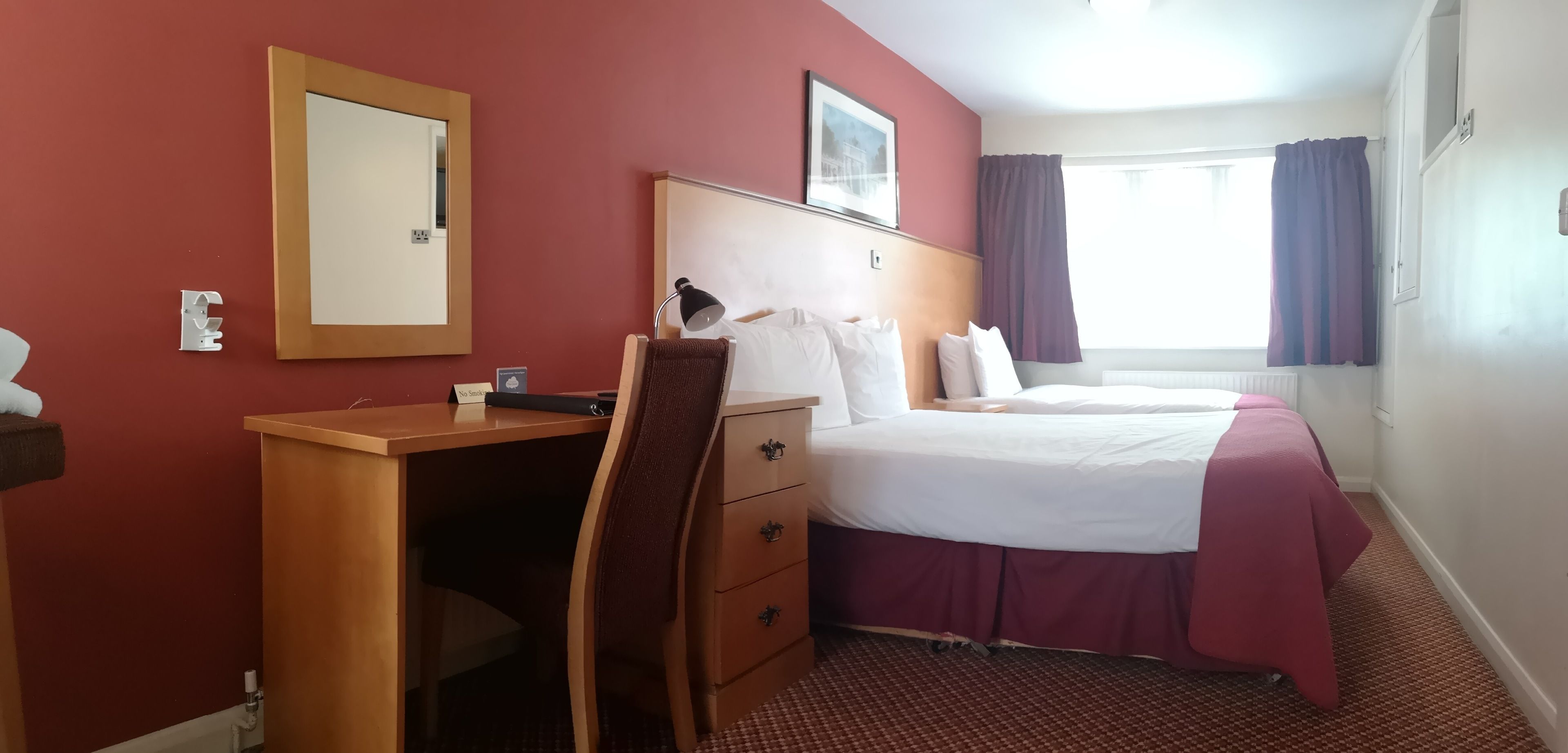 Habitación de hotel con escritorio, dos camas, un espejo grande y una ventana con cortinas.