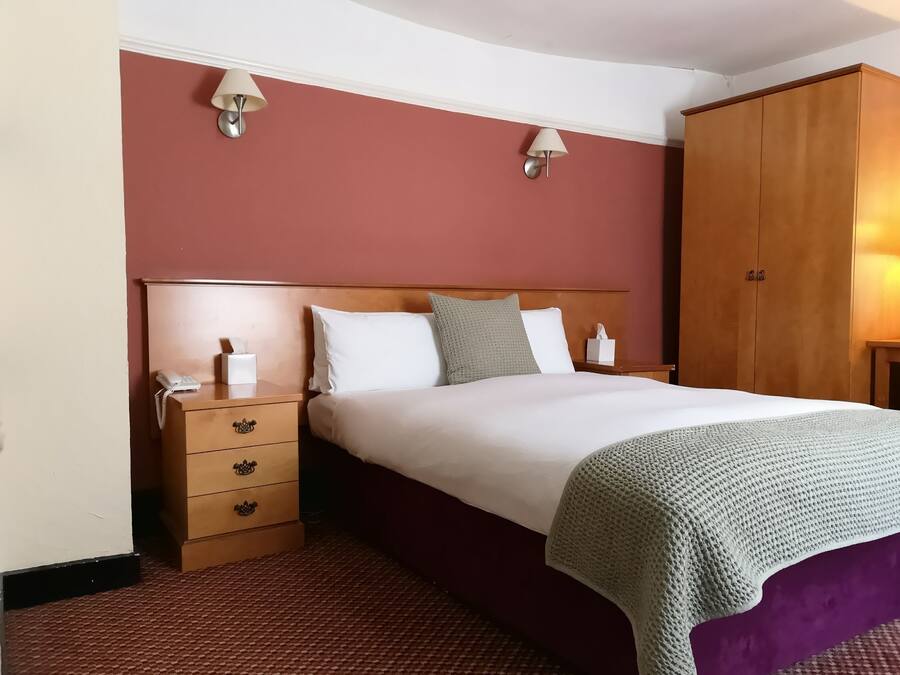 A hotel room with a wooden headboard, a bed with white bedding, two bedside lamps, a wooden wardrobe, and a telephone on the nightstand.