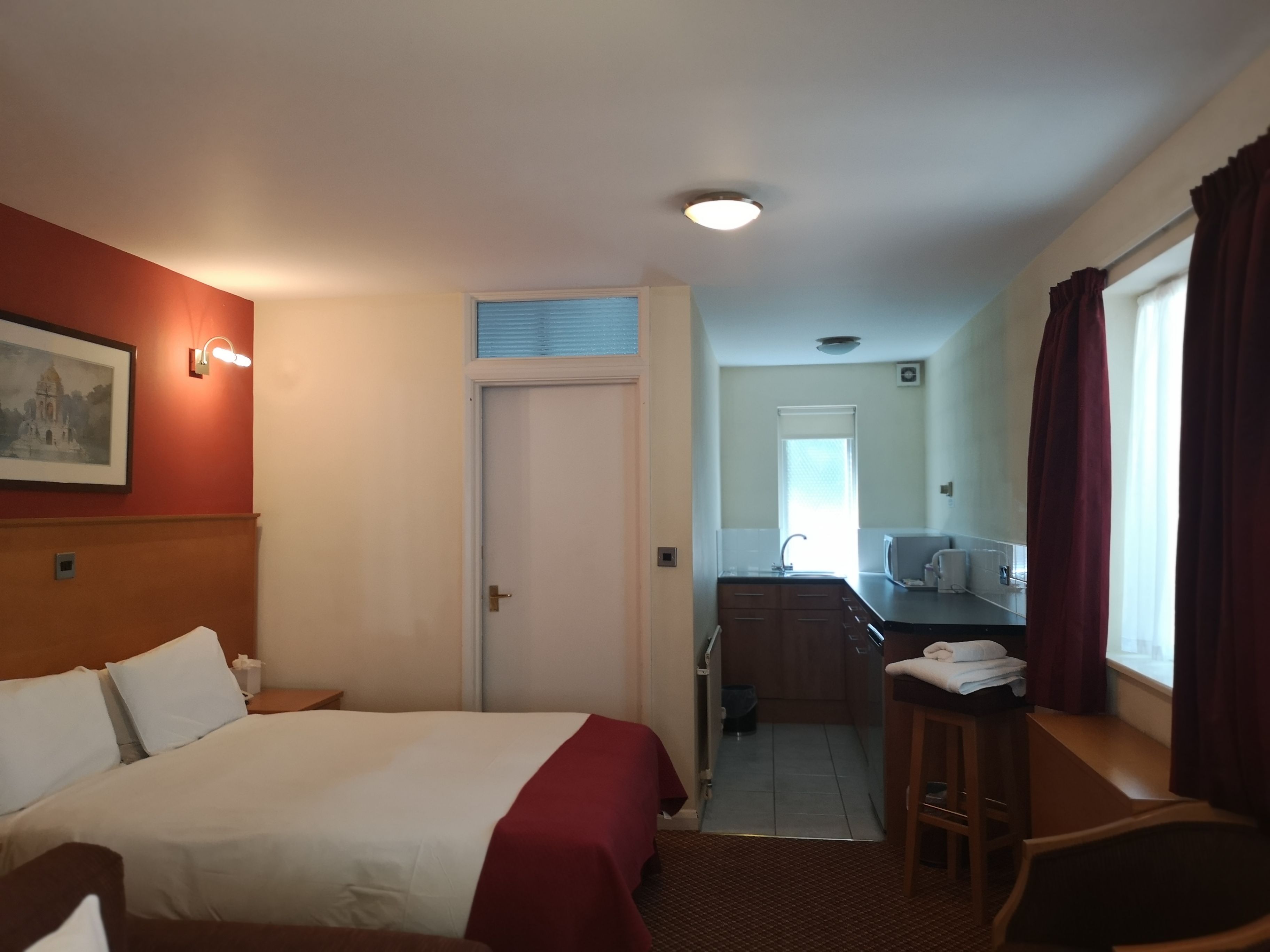 A hotel room with a bed, a desk, a chair, a bathroom, and a window with curtains.