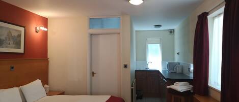 A hotel room with a bed, a desk, a chair, a bathroom, and a window with curtains.