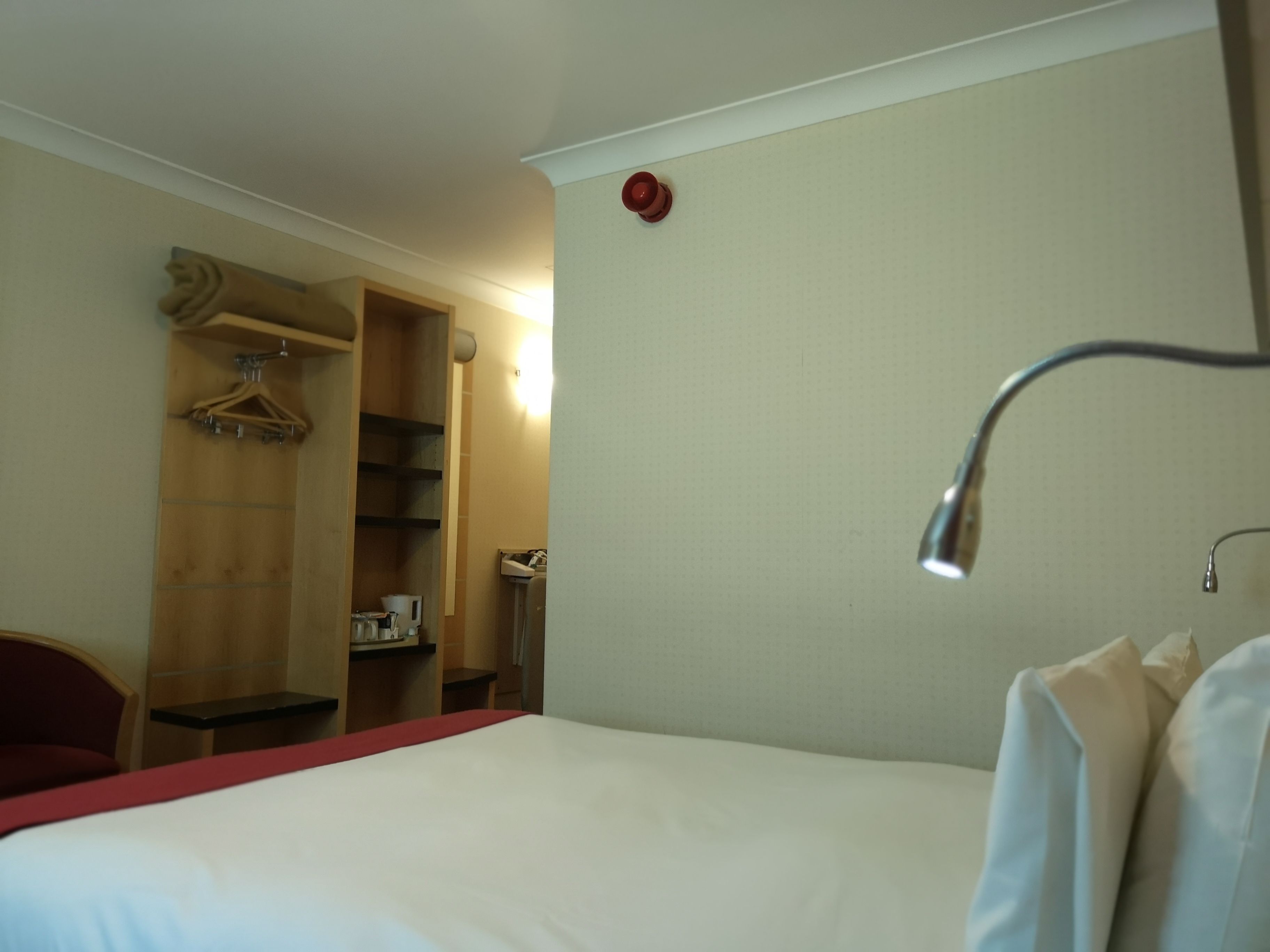 A hotel room with a bed, a wooden wardrobe, a desk, and a mirror.